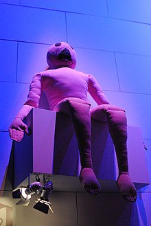Marionnette en tissu en forme d'homme posée sur une boîte grise.