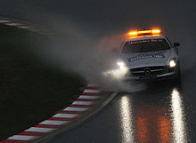 A large amount of water is sprayed from the tyres of a silver sports car with orange hazard lights on the roof.