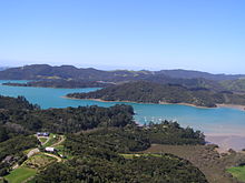 Bild von Natur, das obere Drittel des Bildes ist ausgefüllt vom blauen Himmel. Im mittleren Drittel ist eine Waldlandschaft, durch die sich ein türkisblaues Wasser fließt. Das untere Drittel ist teilweise dunkelgrün durch Bewaldung und hellgrün durch Wiesenlandschaft.