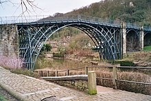 The cast iron Iron Bridge at Coalbrookdale, opened in January 1781 and was the first large-scale object made out of cast iron; but cast iron is not reliably strong due to impurities. Wrought iron, where the carbon is hammered to remove the carbon and impurities is much stronger; the first large-scale wrought iron bridge was the Britannia Bridge over the Menai Strait, only possible due to its innovative box girder design by Robert Stephenson The Iron Bridge - geograph.org.uk - 224230.jpg