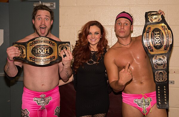 Mike Bennett (left) and Matt Taven (right) displaying their ROH World Tag Team Championship, along with Maria Kanellis-Bennett