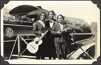 Three young women with a guitar and a ukelele, stand in front of a Hawaii Consolidated Railway steamtrain, Hilo Region, Hawaii, 1929 - C.M. Yonge (16216486554).jpg