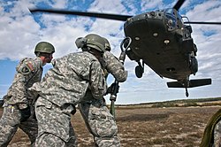 Students at Fort Hood brace against the propwash of a UH-60 Black Hawk as they prepare to attach a slingload during one of the course's practical exercises. Air assault slingload test.jpg