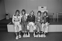 Five young men, two in tartan shirts, all wearing Dutch clogs