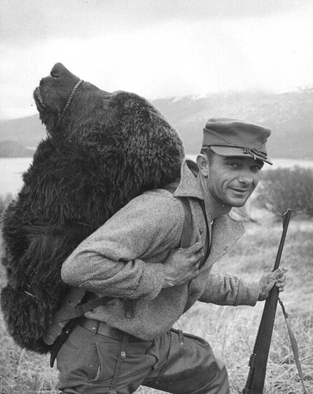Hunter with a bear's head strapped to his back on the Kodiak Archipelago