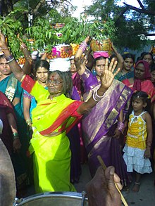 Several women clad in sari, some carrying decorated pots on their head.