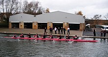 Churchill College Boat Club men's first VIII rowing past their boathouse on the River Cam. The club is noted for its pink boats. Churchill College Boat Club Fairairns M1.JPG