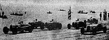 Foto van verschillende voertuigen in dichte formatie bij de start van de Grand Prix.
