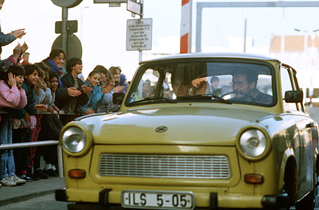 Berlin Duvarının yıkılışını müteakiben Trabant'a binerek Checkpoint Charlie sınır kapısından Batı Berlin'e giren Doğu Almanyalı bir çift ve karşılayan Batı Almanyalı çocuklar (14 Kasım 1989). (Üreten: Lee Cockran)