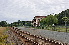 Il single track a scartamento normale, la banchina con il ricovero della sosta.  Sullo sfondo l'ex stazione della rete bretone divenuta proprietà privata