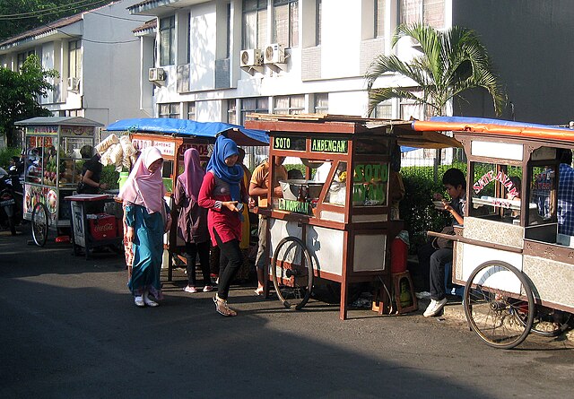 Traditional gerobak food carts lining Jakarta street, selling various Indonesian street foods.