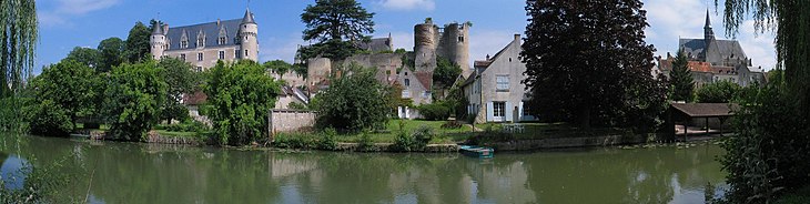Photographie en couleurs d'un château Renaissance, de tours médiévales et d'une église du XVe siècle en arrière-plan d'un village au bord de l'eau.