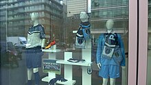 Photographie de la vitrine d'un bâtiment. Des écharpes et des maillots sont exposés.