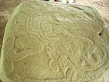 a flat stone with a sculpted bas-relief design. Two clawed feet at the left support a cartouche containing a seated figure, seen from the side with head to the right.