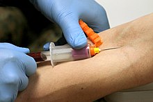 Drawing blood from the median cubital vein using a vacutainer. The clear plastic sheath around the top of the tube holds the needle. The orange guard will shield the needle after it is withdrawn from the patient to protect from accidental needle sticks. USMC-11162010-M-4178N-181.jpg