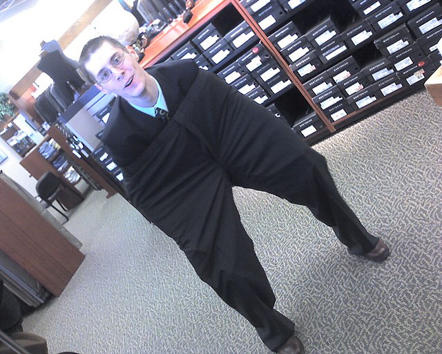 A person working in a retail store wearing a large pair of pants in an attempt to amuse those around them