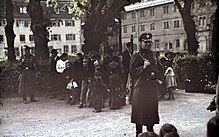 Deux personnes armées en uniforme gardent un groupe d'une quinzaine de personnes composé surtout d'enfants.