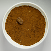 Finely grounded coffee beans in white bowl with intact roasted bean.png