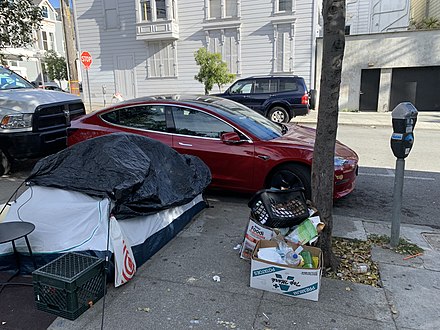 Homeless person in front of a parked Tesla in the Mission District in 2022.