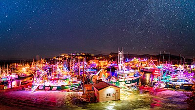 Perayaan Malam Natal di Newfoundland, Kanada, yang mana perahu-perahu dihiasi dengan lampu berwarna warni di bawah langit berbintang.