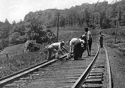 Circa 1917, American section gang (gandy dancers) responsible for maintenance of a particular section of railway. One man is holding a lining bar (gandy), while others are using rail tongs to position a rail.