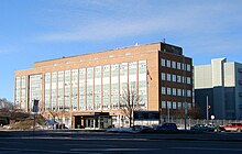 A long rectangular building that appears to be made of red bricks with windows on both the long and short sides