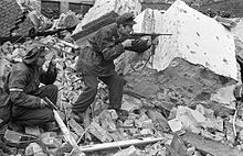 Home Army soldiers Henryk Ozarek "Henio" (left) holding a Vis pistol and Tadeusz Przybyszewski "Roma" (right) firing a Blyskawica submachine gun, from "Anna" Company of the "Gustaw" Battalion fighting on Kredytowa-Krolewska Street, 3 October 1944; the use of pistols in street battles indicates a very poor equipment of weapons of the rebels Warsaw Uprising by Chrzanowski - Henio Roma - 14828.jpg