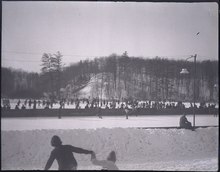 group of persons skating with hockey sticks playing ice hockey on a frozen pond