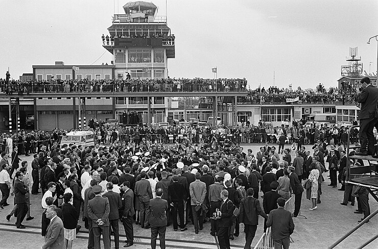 Members of the media swarm the Beatles at Amsterdam's Schiphol Airport in June 1964, as fans await them on top of the airport terminal.