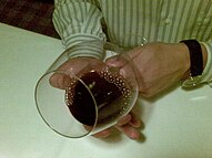 A wine tasting assessing the age of a red wine by tilting the glass forward and observing the rim variation and change of color against a white surface. Assessing the age of a red wine.jpg