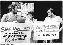 Drei Personen mit zwei Protestplakaten vor einer Tordurchfahrt