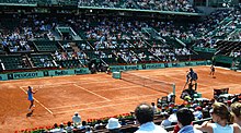 The French Open, played on red clay, is one of four Grand Slams in professional tennis. Court Philippe Chatrier Ana Ivanovic 2009 (3577046132).jpg