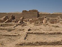 Photo en couleur. Dans le désert, des vestiges en pierre sont à l'avant-plan.