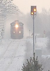 A Finnish distant signal at the western approach to Muhos station is displaying Expect Stop. In the background, express train 81 is pulling away from the station. Finnish distant signal displaying Expect Stop.jpg