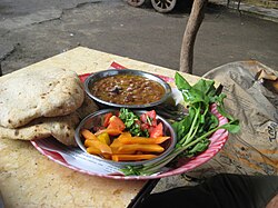 Typical fūl medames breakfast as served by an Egyptian street vendor with bread and pickled vegetables, as well as fresh rocket (arugula) leaves on the side.