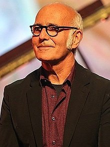 Ludovico Einaudi male wearing glasses and a black jacket, smiling and looking right of camera