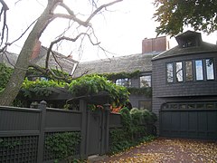 A brown shingled house is obscured by a wooden fence and an arbor.