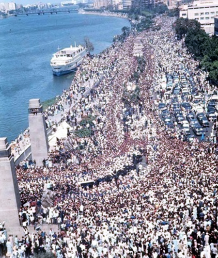 Throngs of people marching in a thoroughfare that is adjacent to a body of water