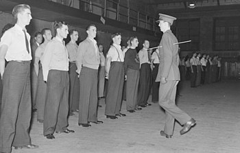 An officer of the Canadian Grenadier Guards demonstrates how to turn about to a group of recruits in civilian clothes, 1940.