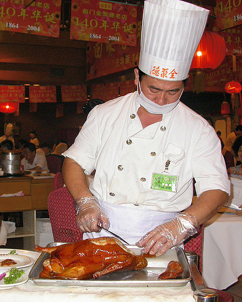 A Quanjude cook is slicing Peking roast duck. Peking duck is eaten by rolling pieces of duck with scallion, cucumber and sweet bean sauce using steame