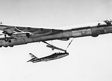 Un petit avion de chasse est accroché à un trapèze sous un gros bombardier.