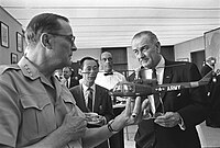 Generál Earle Wheeler drží model helikoptéry U.S. Army v provedení ambulance. Vu Van Thai a prezident Lyndon B. Johnson jej pozorují, 8. února 1966.