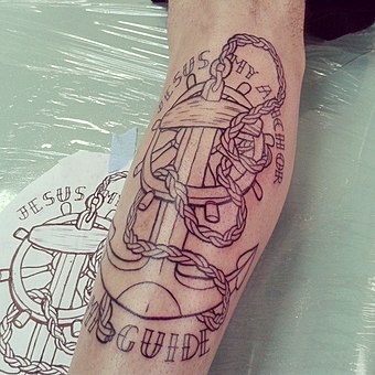 A sailor's forearm tattooed with a rope-and-anchor drawing, against the original sketch of the design; see sailor tattoos