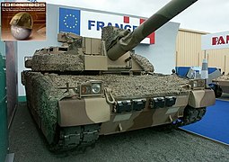 Un char beige et marron exposé dans un salon militaire, en extérieur, devant une pancarte « France ».