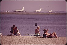 Playa en primer plano, aeropuerto al fondo.