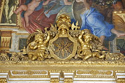 Photographie de la jonction entre les murs et le plafond. Un trumeau doré avec des angelots encadrant un écu où sont représentés les insignes de Jupiter : la foudre et les éclairs