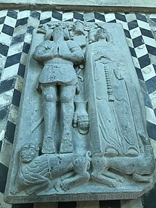 Gisant en pierre représentant un homme en armure médiévale et une femme en robe. À leurs pieds, un lion et un chien.