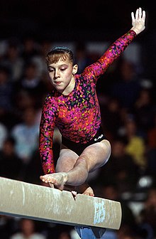 Une jeune fille sur une poutre de gymnastique, vêtue d'un justaucorps à dominante rose.