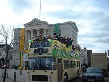 A group of men are standing on the top level of a double-decker bus.