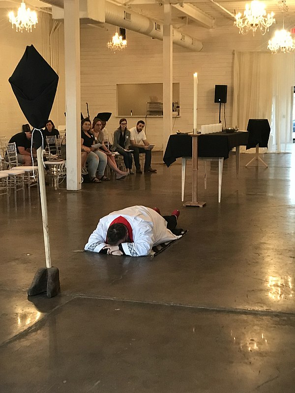 During a Good Friday liturgy, a Christian clergyman prostrates himself in accordance with the rubrics in the Book of Worship. The processional cross i